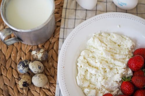 Top view of a rustic breakfast with milk, quail eggs, cottage cheese, and strawberries on a woven mat.