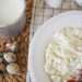 Top view of a rustic breakfast with milk, quail eggs, cottage cheese, and strawberries on a woven mat.